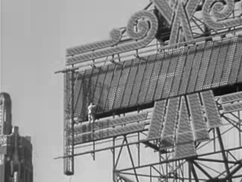 A worker maintaining a large illuminated outdoor sign structure.