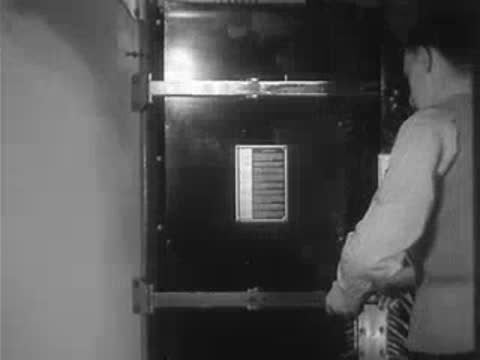 A worker adjusting settings on a large electrical control panel door.