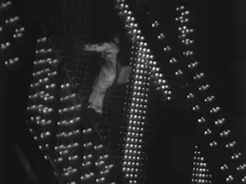 Medium shot of a worker climbing down a massive illuminated sign structure.