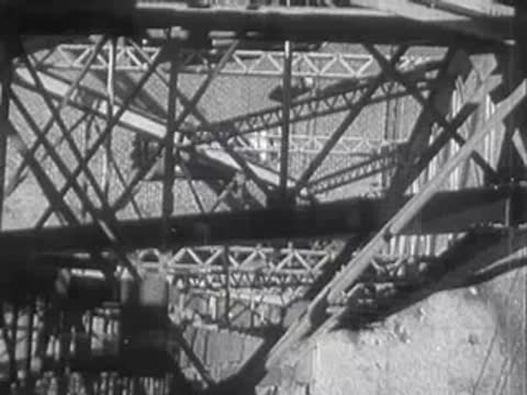 Metal truss bridge structure during the day with city below.