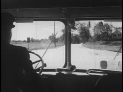 View through a bus windshield looking out at a rural road and trees.