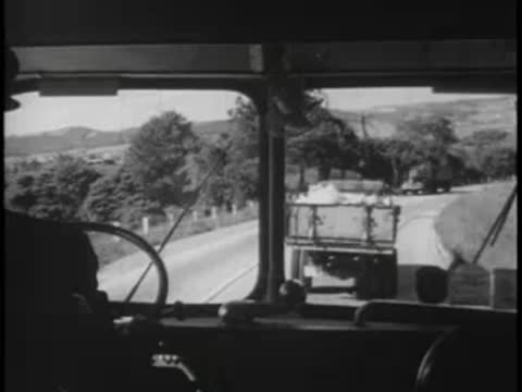 View through a bus windshield of a truck ahead on a winding road.