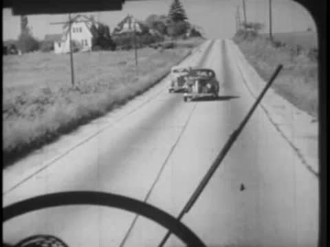 View through a bus windshield as cars pass on a country road.