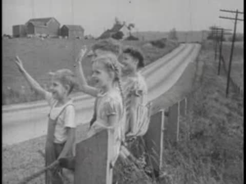 Children waving from roadside as bus passes, rural setting.