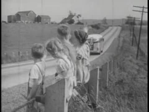Children waving at bus driving away on country road.