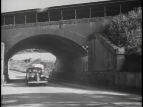 Bus driving under stone bridge on country road, 1940s.