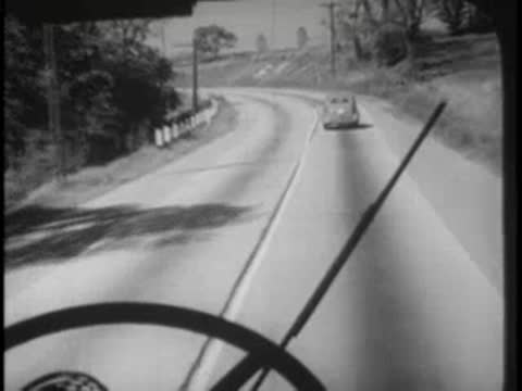Bus interior view of winding road through trees, steering wheel.