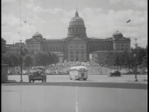 Bus driving past large capitol building with dome, city street.
