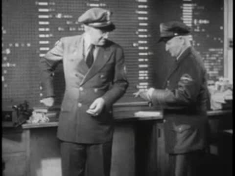 Two men in bus driver uniforms talking in dispatch office.