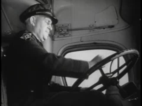 A bus driver in uniform holding the steering wheel inside the vintage cab.