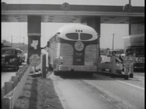 A vintage passenger bus driving through a toll plaza booth with attendants.