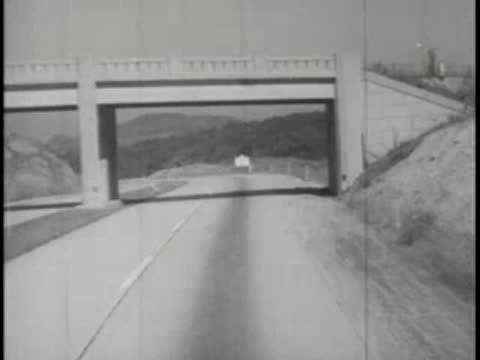 View from inside a bus passing underneath a concrete highway overpass bridge.