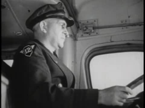 Bus driver in uniform and cap looking ahead while driving with hands on wheel.