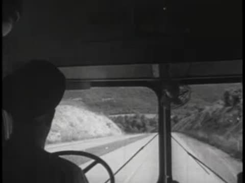 Driver's view looking down a divided mountain highway with bright sunlight ahead.