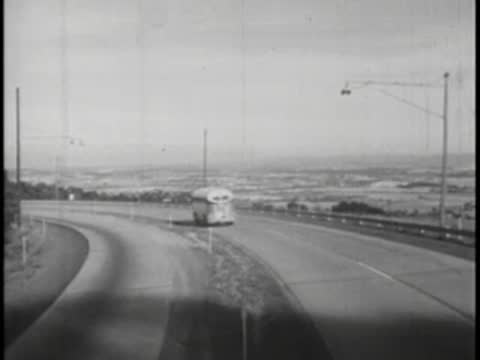 A bus traveling away down a curved multi-lane highway in a valley.