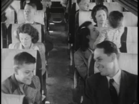 Passengers inside bus, seated and talking, period clothing.