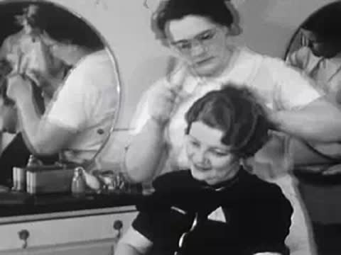 Stylist styling a woman's short curly hair in front of a mirror.