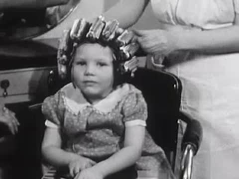 Young girl sitting with curlers in her hair, smiling slightly.