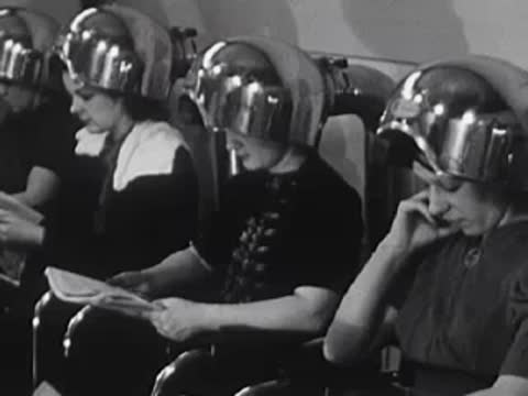 Customers sitting under hair dryers reading magazines in the salon.