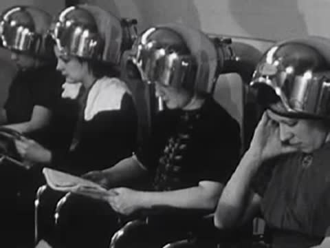 Customers under hooded hair dryers in the salon setting.