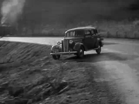 1930s sedan driving along a winding rural road in autumn