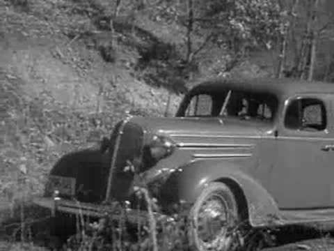 Sedan parked near a wooded riverbank with bare winter trees