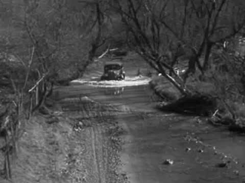 Sedan driving down a shallow rural riverbed with sparse trees