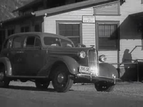 1930s sedan parked in front of a light-colored wooden building