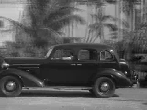 1930s sedan parked in a sunny tropical location with palm trees