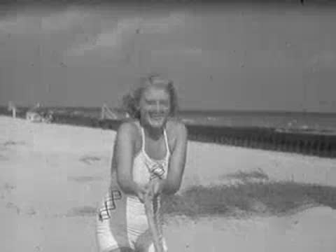 Smiling woman in 1930s swimsuit holding a rope on a beach