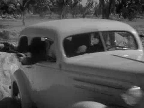 A car drives rapidly through dusty, sandy terrain with palm trees.