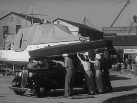 Men load a small boat onto the roof rack of a car.