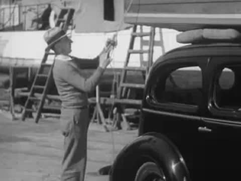 A man secures a boat onto the roof rack of a car.