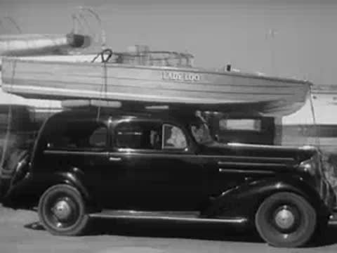 A car with a boat on its roof drives along a road.