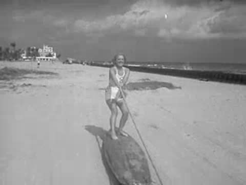 Woman in swimsuit pulling a rope connected to a surfboard on sand
