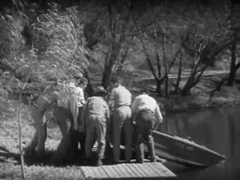Men launch a boat into a calm river from a wooden dock.