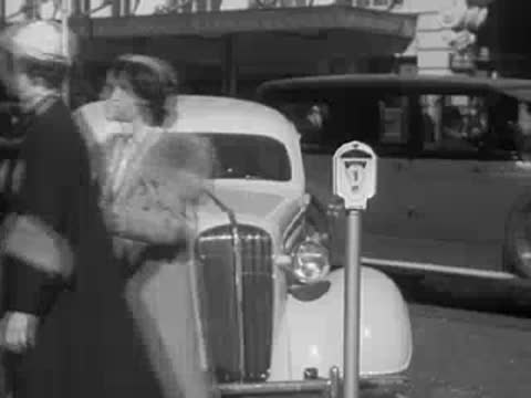 Women walk on a sidewalk past a parked car and parking meter.