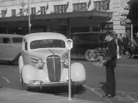 A parking meter stands on a city sidewalk near a parked car.