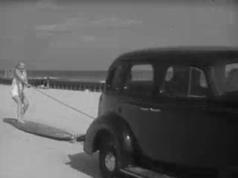 Close-up of a car tire transitioning to a woman pulling a surfboard