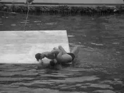 men wrestle and tumble off a floating mat into the pool