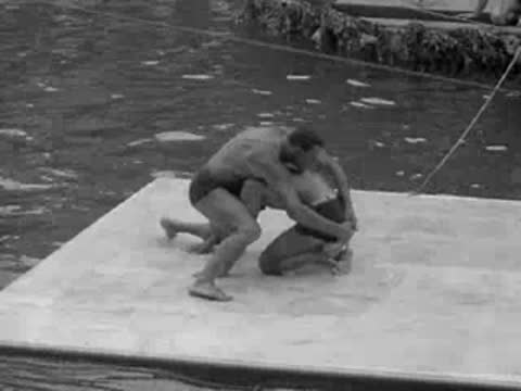 men grapple and wrestle on a floating mat in a pool