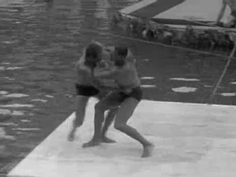 two men grapple on a floating mat before falling into the pool