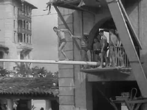 a man runs across a long horizontal pole suspended over a pool