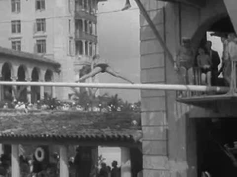 a man performs acrobatics on a long pole above a swimming pool