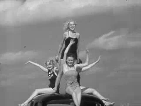 Three women posing on top of a 1930s car roof on a beach
