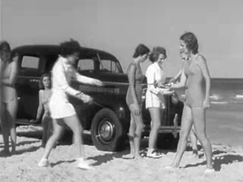Group of people in swimsuits and fencing gear near parked car on beach
