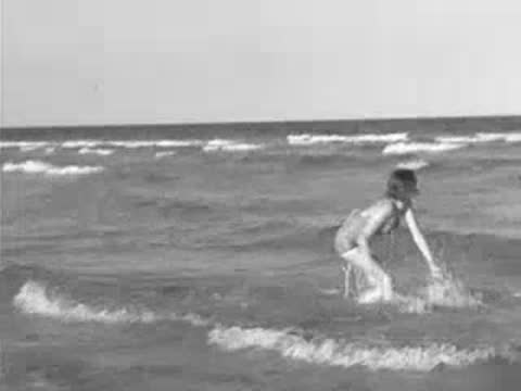 Parked car on beach, woman running out of ocean surf