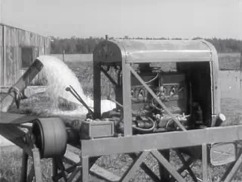 A large industrial water pump operates in a rural landscape near a building.