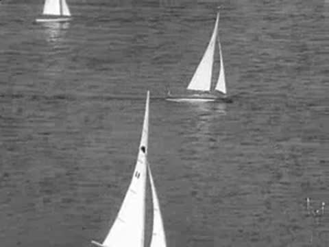 A fleet of small model sailboats races across a calm body of water.