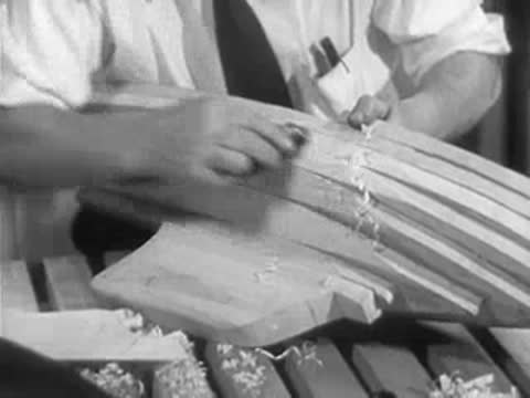 A craftsman sands and scrapes the wooden hull of a model sailboat.